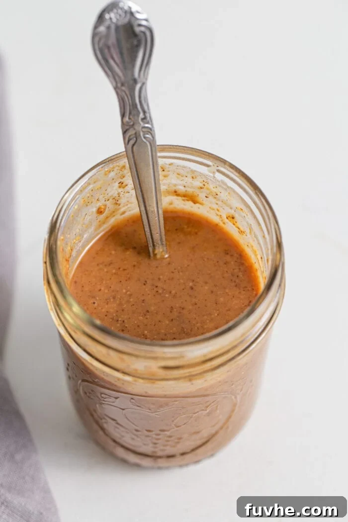 Creamy coconut almond butter sauce in a jar with a spoon resting in jar.