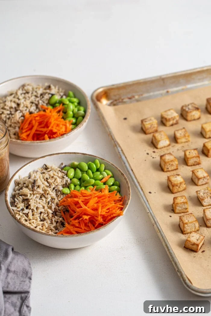 Bowl of rice, carrot and edamame sitting beside a baking tray of tofu.