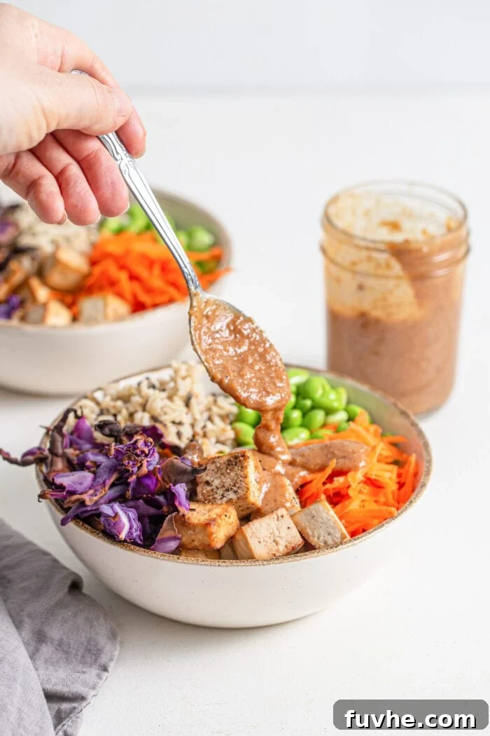 Hand spooning sauce over a colourful bowl of rice, tofu and vegetables.