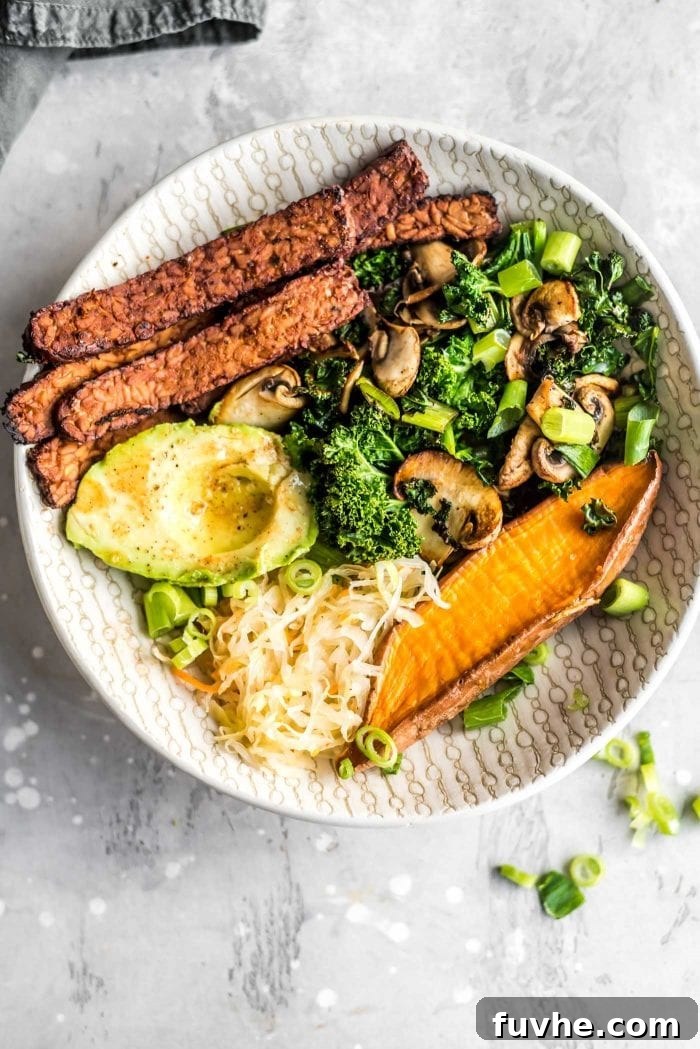 Overhead shot of a vibrant vegan tempeh bacon, avocado, kale and mushroom sweet potato breakfast bowl, perfectly arranged and ready to eat, highlighting its fresh and wholesome ingredients.