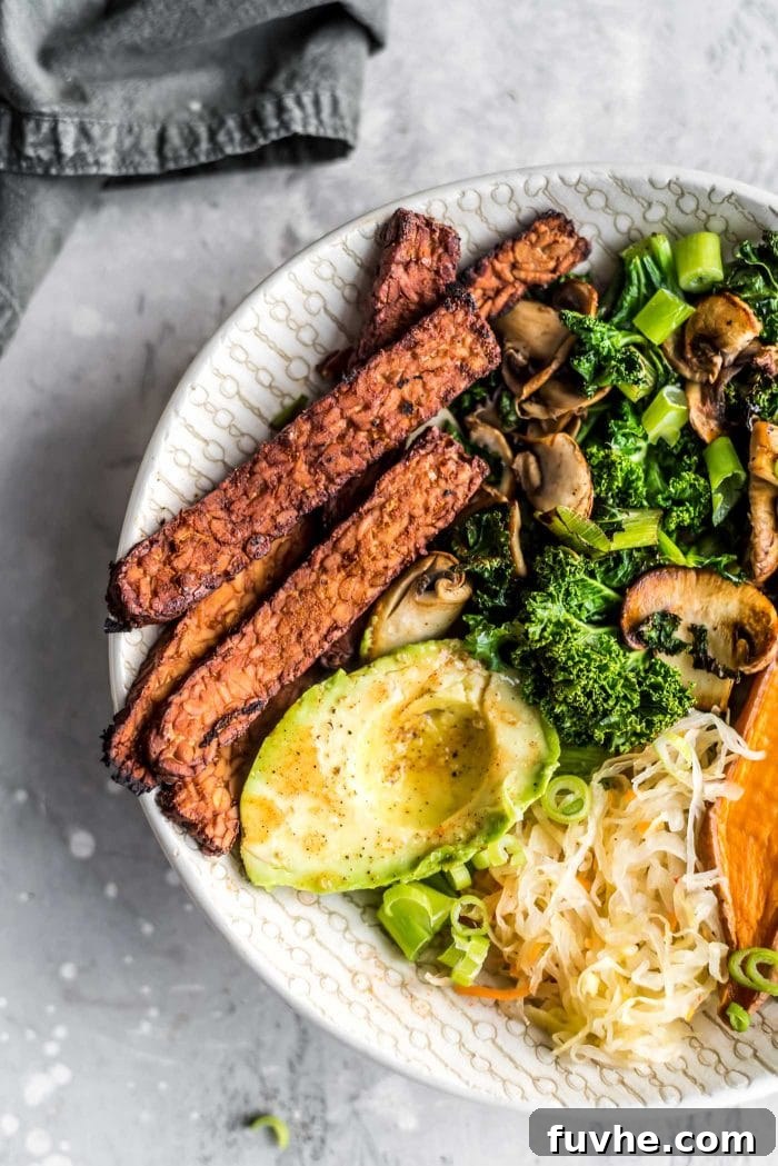 Close-up view of perfectly crispy, golden-brown homemade tempeh bacon strips, freshly cooked and glistening, arranged in a savory vegan breakfast bowl, highlighting its appealing texture.