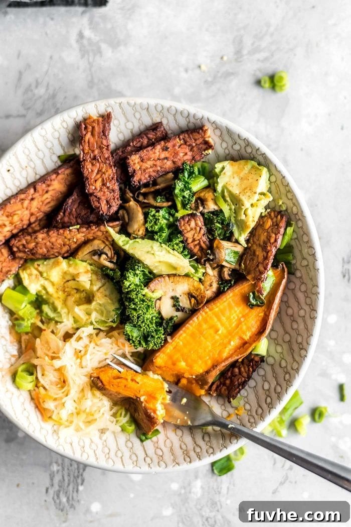 A beautifully arranged, close-up shot of a savory breakfast bowl showcasing cooked tempeh bacon, creamy avocado slices, vibrant roasted sweet potato cubes, a generous dollop of tangy sauerkraut, fresh green kale, and tender sautéed mushrooms.