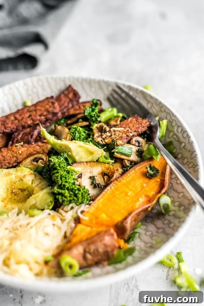 A colorful and appetizing vegan avocado breakfast bowl showcasing tender, cubed sweet potato alongside a generous scoop of vibrant sauerkraut and crispy tempeh bacon slices, ready for enjoyment.