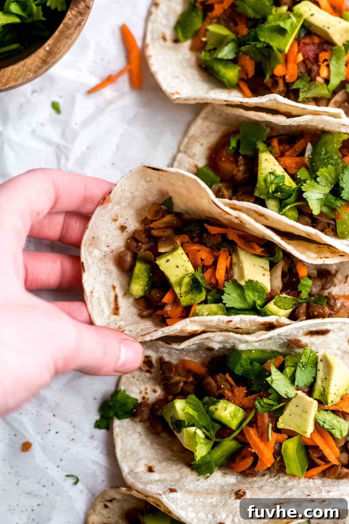 Hand picking up a perfectly garnished vegan lentil taco with fresh avocado, shredded carrots, and vibrant salsa, ready to be enjoyed.