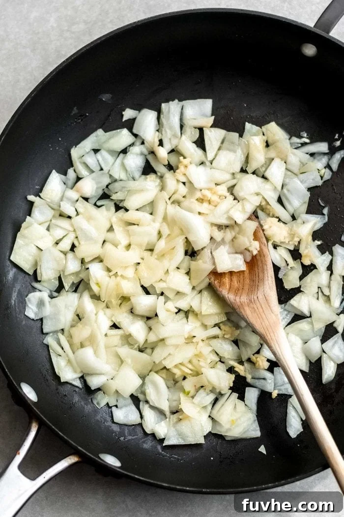 Sautéed onions and garlic sizzling in a black skillet with a wooden spoon, releasing their fragrant aromas.