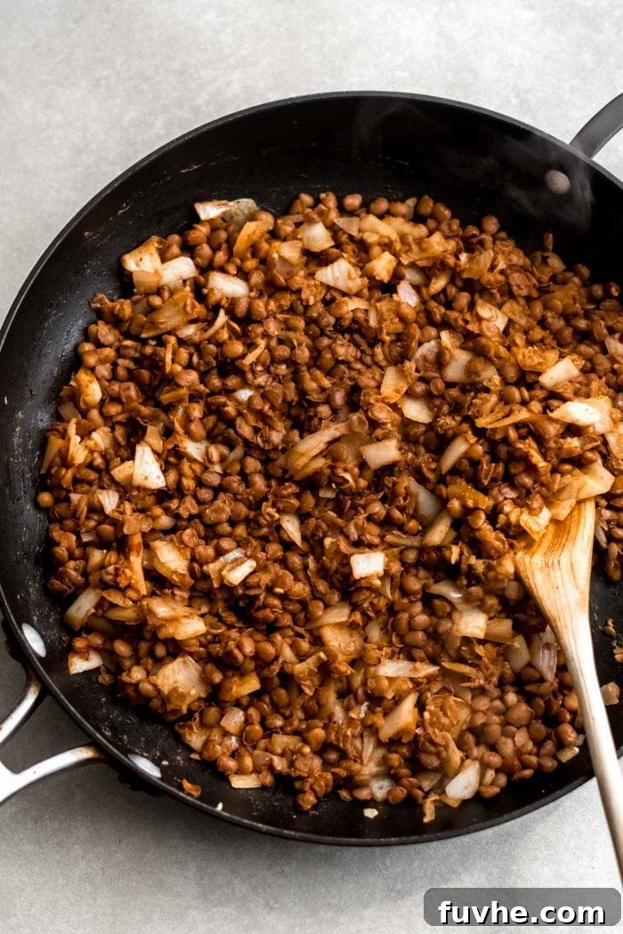 Delicious vegan lentil taco filling simmering in a skillet, being mashed with a wooden spoon to achieve the perfect texture.
