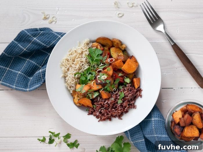 The Ultimate Vegan Macro Cheat Sheet 3 A bowl brimming with wholesome carbohydrate sources like brown rice, sweet potato, and wild rice, alongside a blue napkin and fork on a rustic wood background.