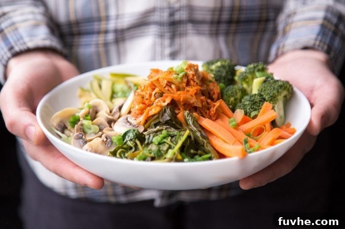 The Ultimate Vegan Macro Cheat Sheet 5 A person gently holding a bowl filled with a colorful and nutritious array of non-starchy vegetables and fermented foods, including vibrant carrots, kimchi, crisp broccoli, leafy greens, and earthy mushrooms.
