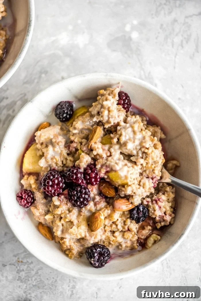 Oven baked steel cut oats in a small bowl with blackberries, maple syrup, almond milk and almonds, ready to be enjoyed.