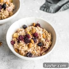 Oven baked steel cut oats in a small bowl with blackberries, maple syrup, almond milk and almonds.