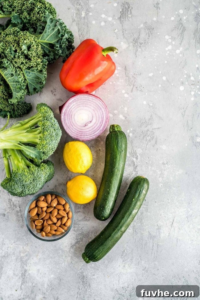 Vibrant Chickpea Garden Salad 3 A vibrant selection of ingredients for chickpea veggie salad, including zucchini, bell pepper, almonds, lemons, fresh kale, and red onion, arranged on a textured surface.