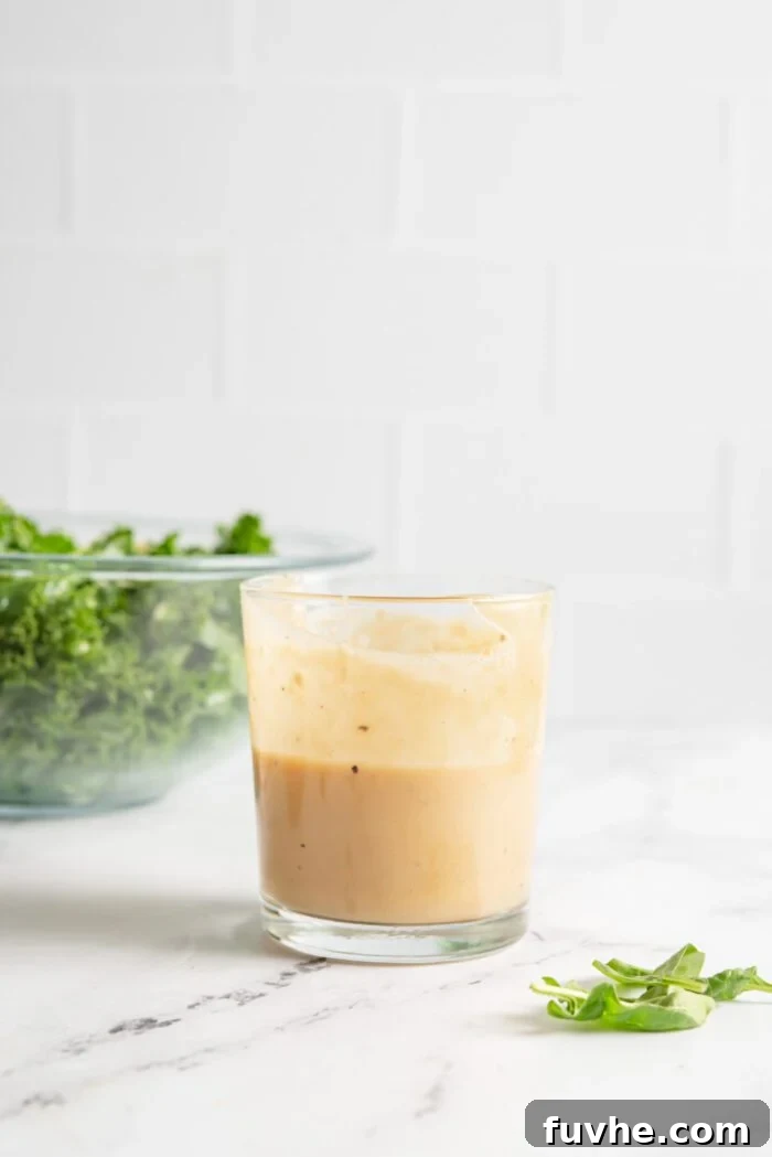 Vibrant Chickpea Garden Salad 6 A jar of creamy tahini maple dijon mustard dressing sitting on a marble counter with a bowl of chopped kale in the background, ready to be combined.