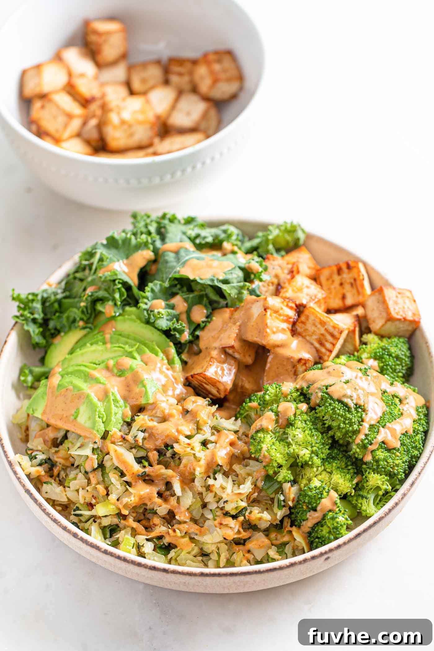 Wholesome Vegan Carb-Conscious Bowls 2 A beautifully arranged low-carb vegan dinner bowl featuring roasted tofu, 'riced' cabbage, steamed broccoli florets, fresh kale, and sliced avocado, generously drizzled with a rich almond satay sauce.