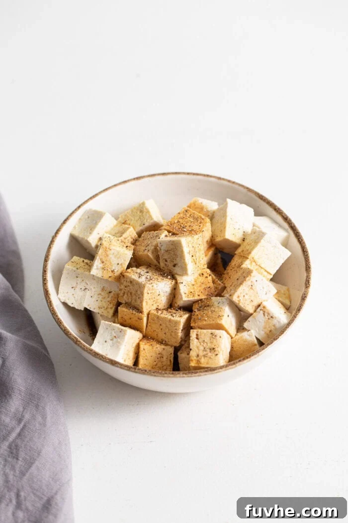 Wholesome Vegan Carb-Conscious Bowls 5 Cubed tofu pieces coated with garlic powder and black pepper in a mixing bowl, ready for baking.