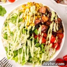 Overhead view of a BBQ tempeh bowls with lettuce, corn, tomato, rice and avocado dressing drizzled over top.