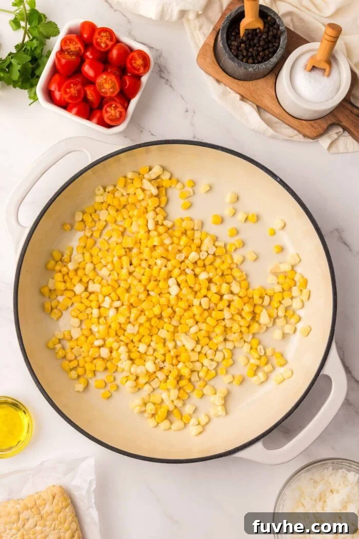 Corn kernels charring in a hot pan, alongside a bowl of fresh tomatoes, ready for assembly.