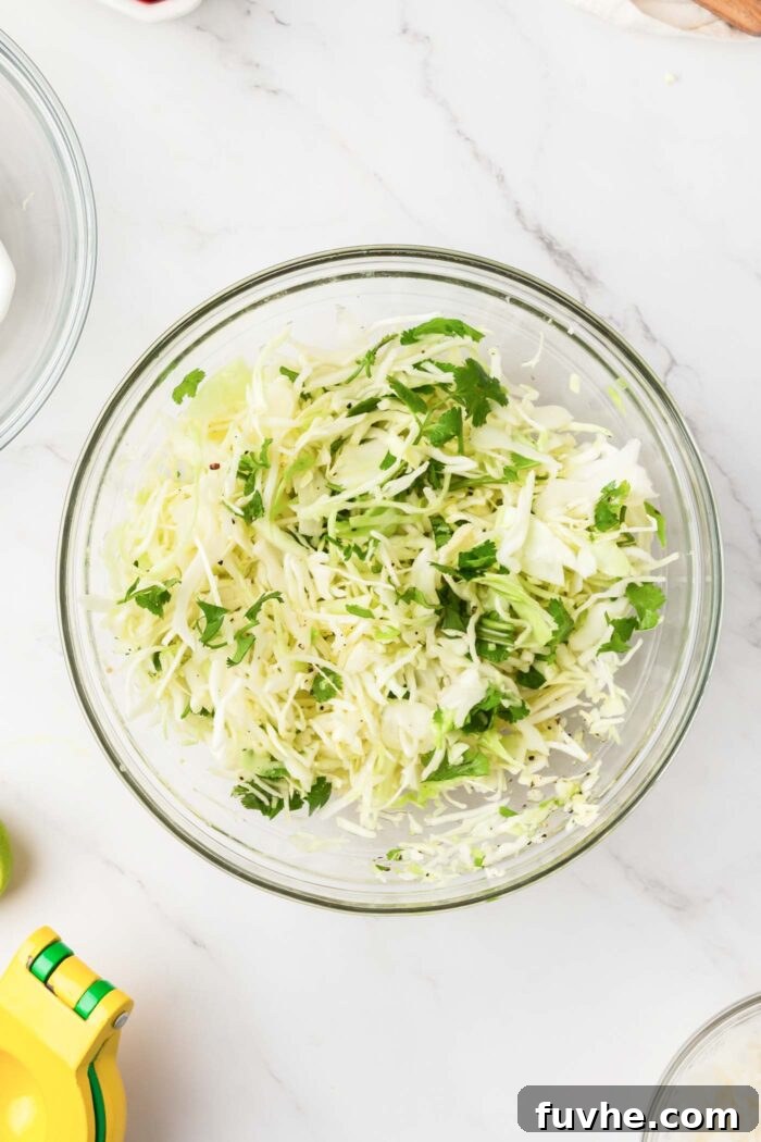 Shredded cabbage and fresh cilantro being mixed in a clear glass bowl, forming the base of the slaw.