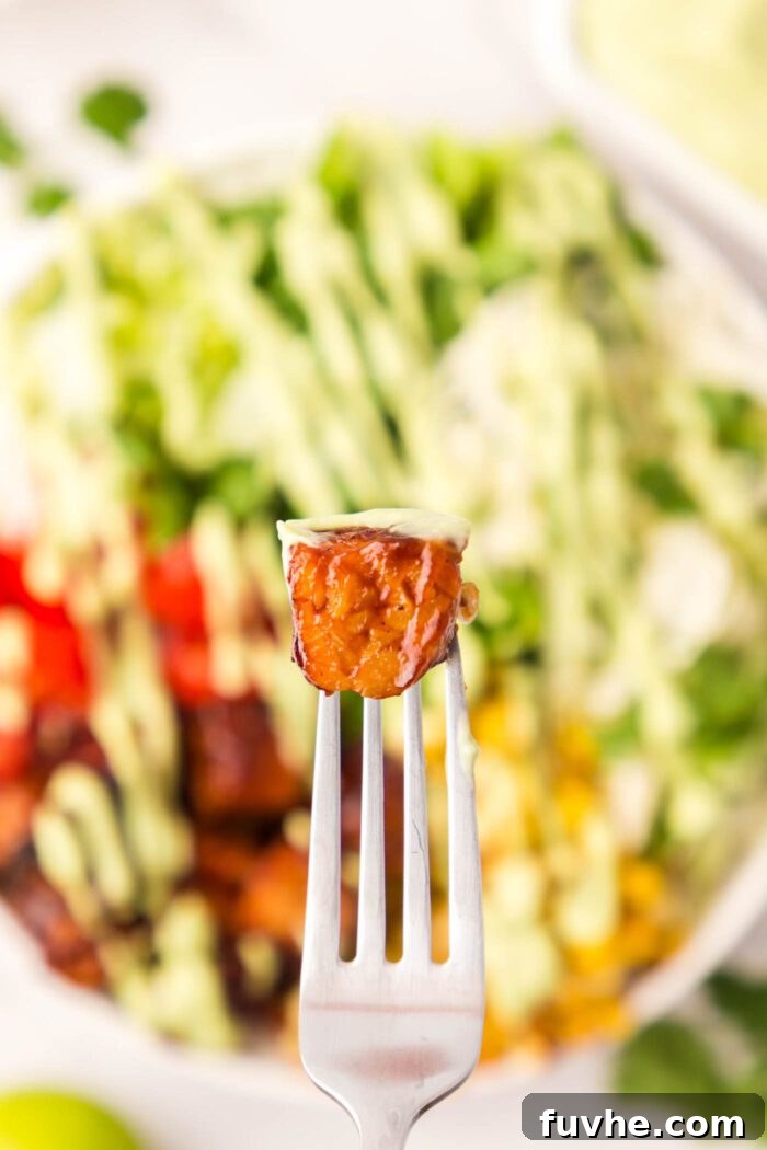 A delicious cube of BBQ tempeh held on a fork, poised over a vibrant, fresh salad bowl.