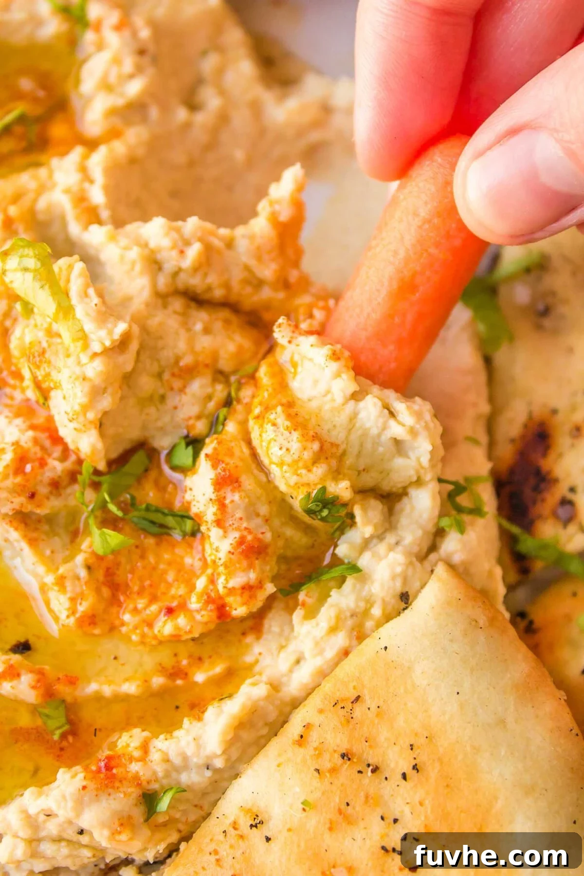 Snack Smarter: 31 Plant-Based Bites 6 A carrot being dipped into hummus drizzled with olive oil.