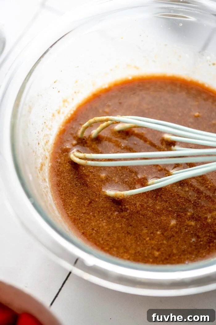 Golden Tempeh Wok Medley 4 A small glass mixing bowl filled with a rich, creamy stir fry sauce, with a whisk resting inside it. The sauce has a deep, inviting color, ready to be incorporated into the stir fry.