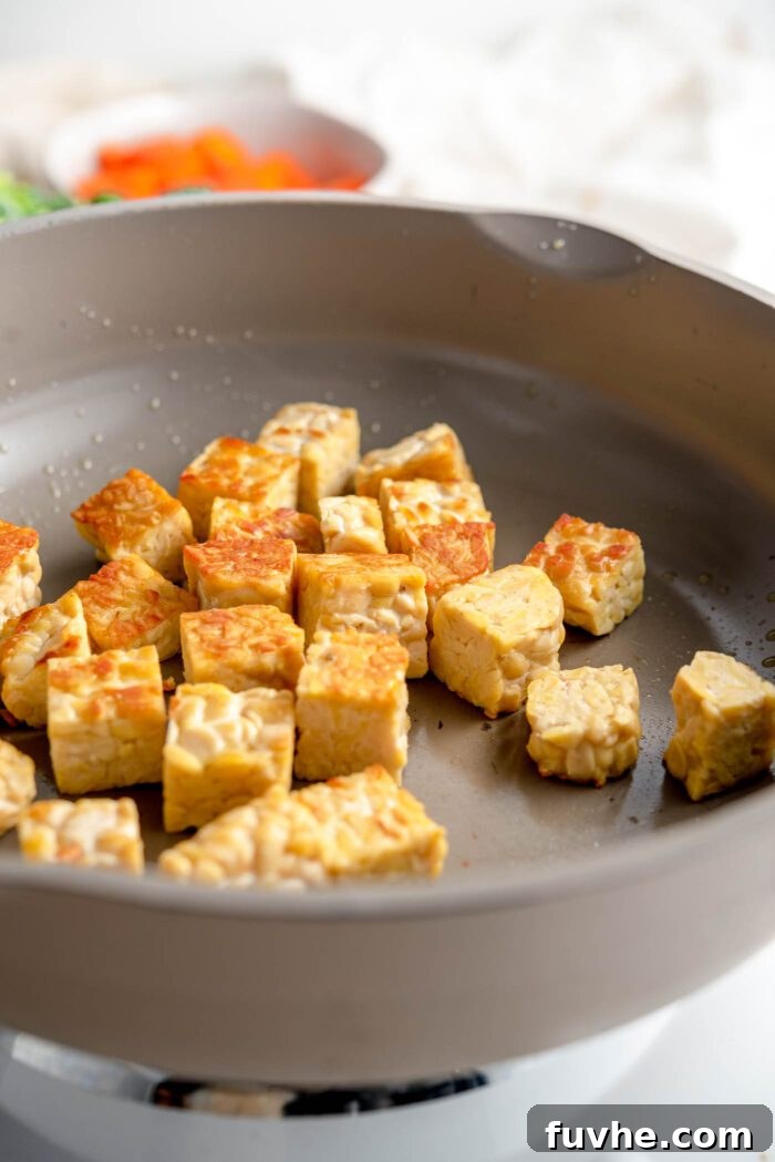 Golden Tempeh Wok Medley 5 Crispy, golden-brown cubes of tempeh cooking in a hot skillet on a stovetop. The tempeh pieces are evenly spaced, showcasing their appetizingly browned surfaces.