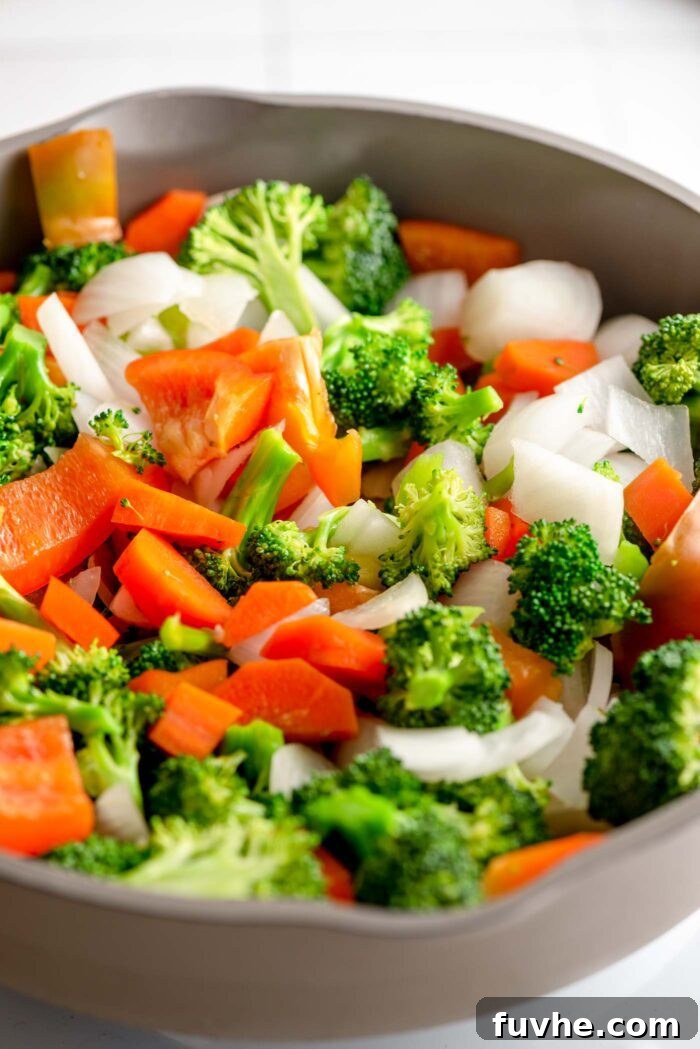 Golden Tempeh Wok Medley 6 A vibrant mix of stir-fried broccoli florets, red bell pepper strips, sliced carrots, and chopped onions cooking in a skillet. The vegetables are colorful and look tender-crisp.