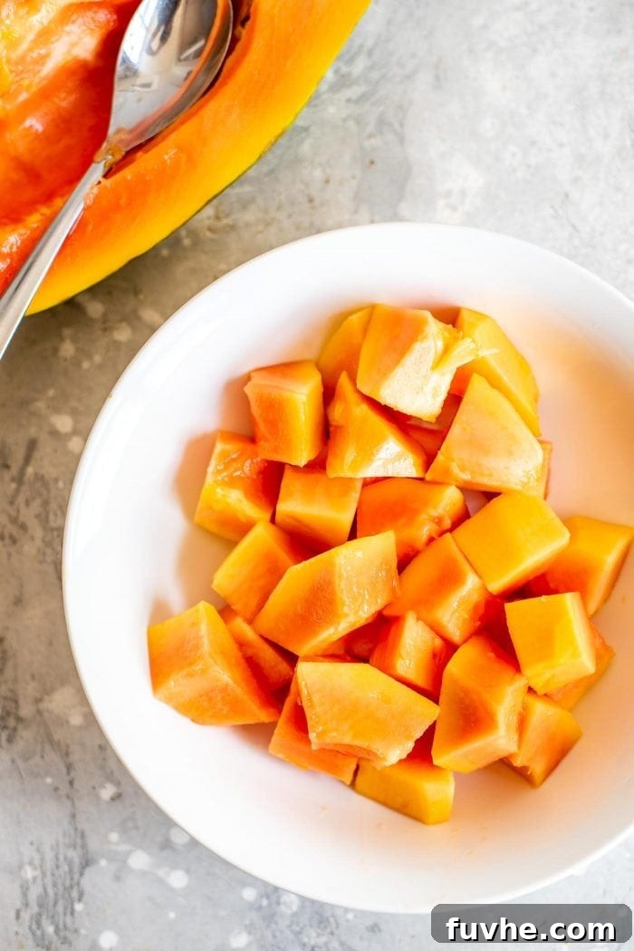 A pristine white bowl filled with beautifully chopped, ripe papaya chunks, showcasing the vibrant orange color and smooth texture of the fruit.