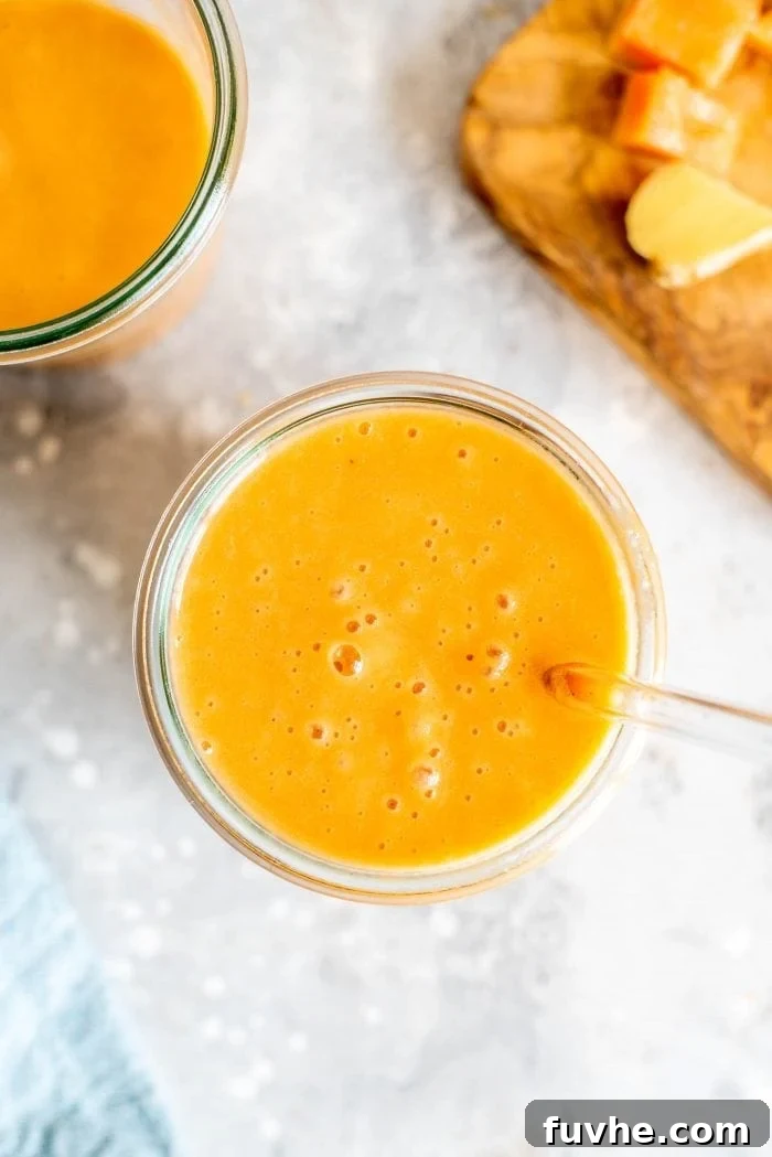 A single glass filled with a vibrant orange papaya and carrot smoothie, complete with a straw, set against a blurred background, emphasizing its refreshing appeal.