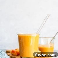 Healthy Creamy Vegan Papaya Smoothie in a glass on a cutting board with some chopped pieces of papaya and ginger.