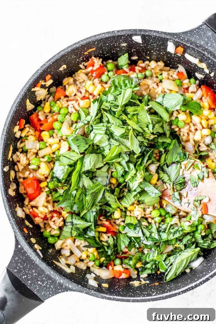 A black skillet filled with sizzling vegan fried rice, highlighted by vibrant green fresh Thai basil leaves.