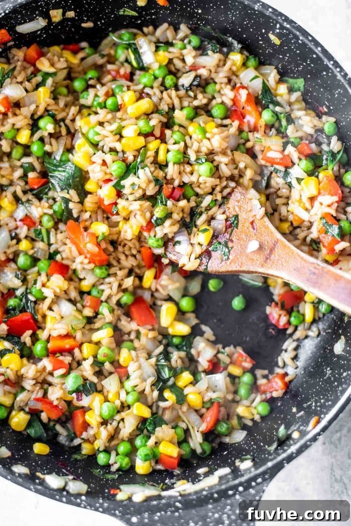 A black skillet presenting a close-up of beautifully browned Vegan Basil Fried Rice, with visible grains and vegetables.