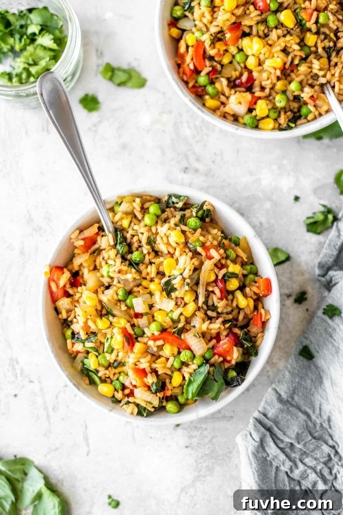 Two white bowls generously filled with healthy vegan basil fried rice, garnished with fresh basil leaves, featuring visible peas, corn, onions, and bell pepper, presented on a light surface.