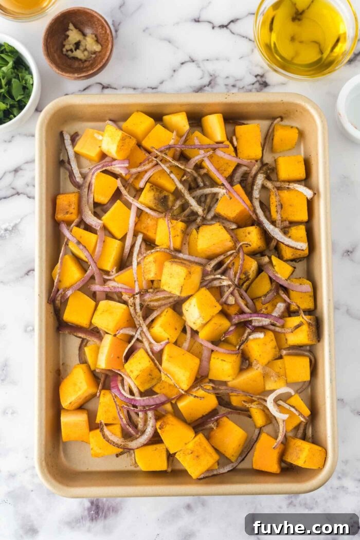 Cubed butternut squash and sliced red onion roasting on a baking tray until golden and tender.