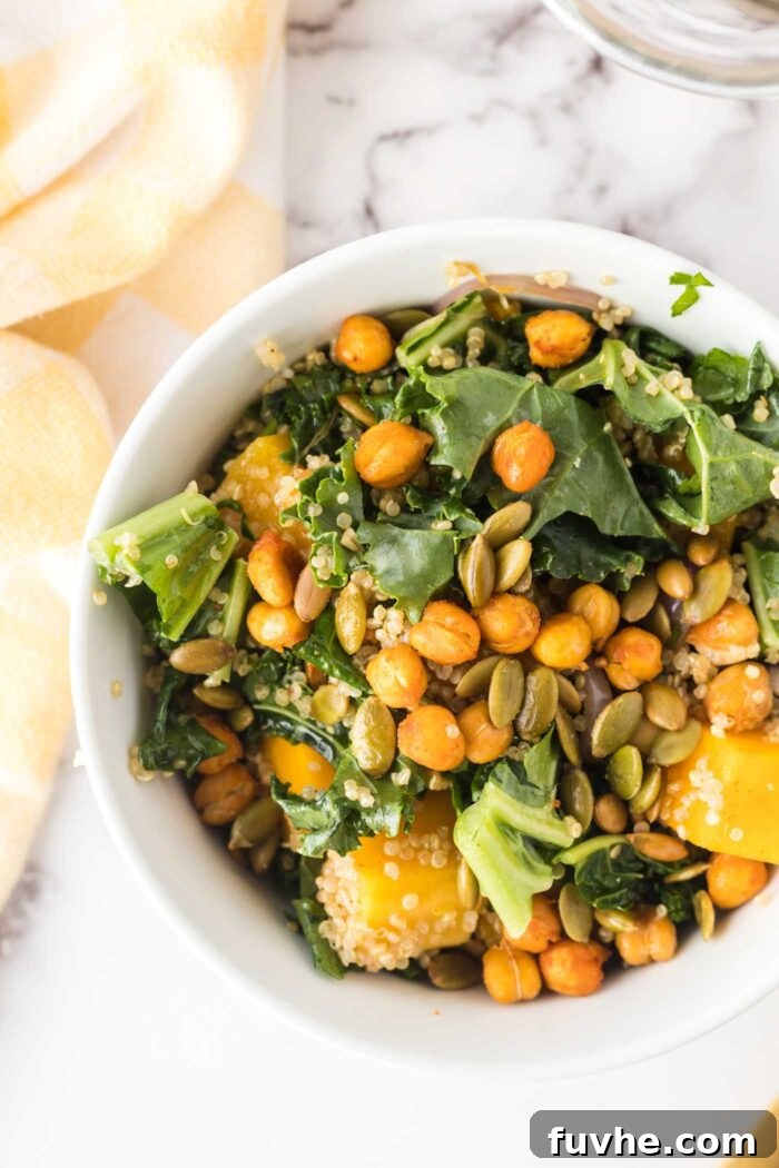 A small, beautifully presented bowl of roasted butternut squash quinoa salad, garnished with crispy roasted chickpeas and toasted pumpkin seeds.
