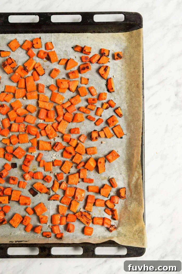 Cubes of squash and carrot on a roasting tray lined with parchment paper, ready for the oven.