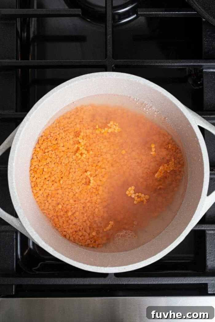 Red lentils cooking in a large pot on a gas range stovetop, simmering gently.