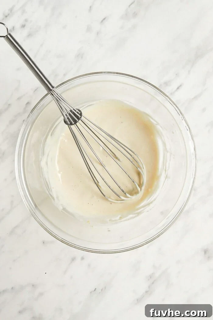 Creamy tahini sauce in a glass mixing bowl with a metal whisk, ready to be drizzled.