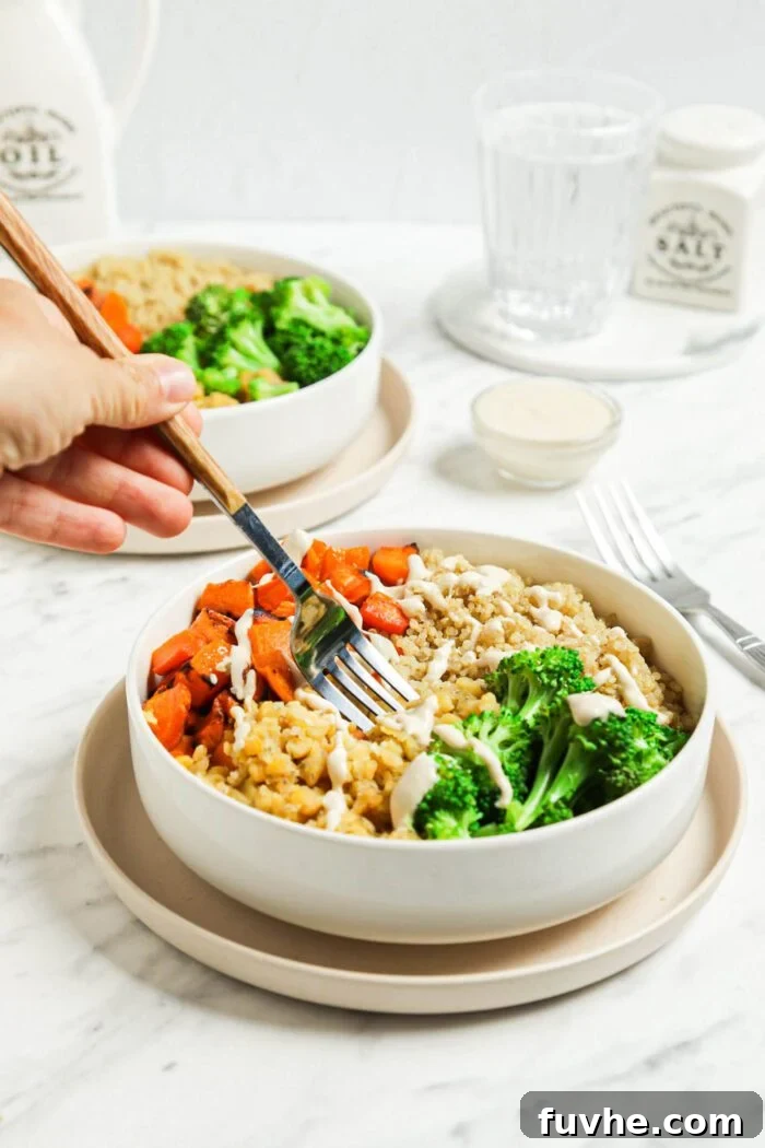 Hand using a fork to dig into a healthy lentil and quinoa bowl with roasted squash and broccoli, invitingly ready to eat.