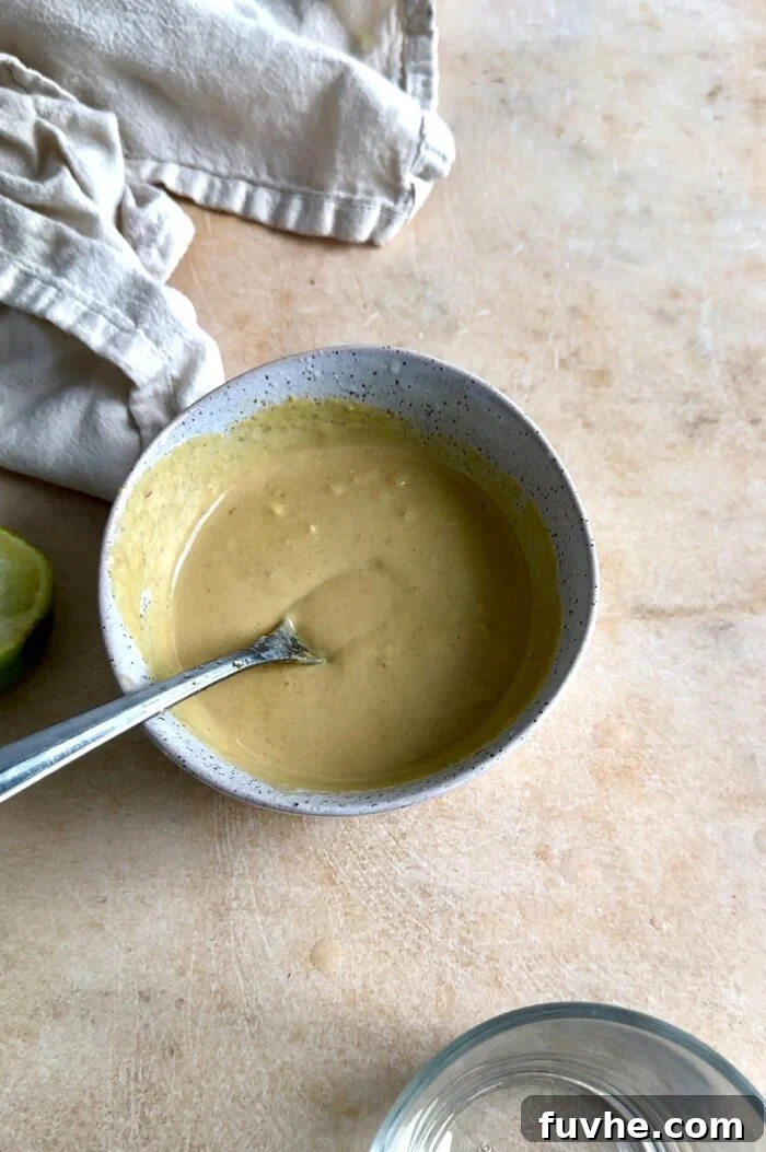 A small bowl of creamy chipotle tahini dressing, garnished with a spoon, showcasing its rich and smooth texture.