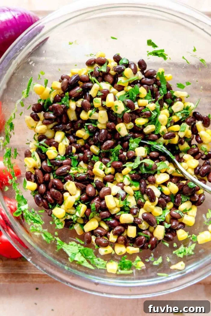 A glass bowl containing a vibrant mixture of black beans, corn, and fresh cilantro, seasoned and ready for the taco salad.