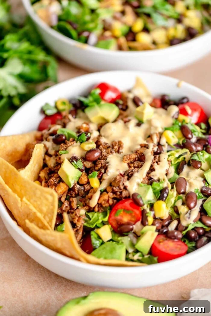 A beautifully assembled bowl of vegan taco salad, featuring a generous drizzle of creamy dressing over the mushroom-walnut crumbles, fresh lettuce, juicy tomatoes, creamy avocado, black beans, red onion, and corn. Tortilla chips are served on the side for scooping.