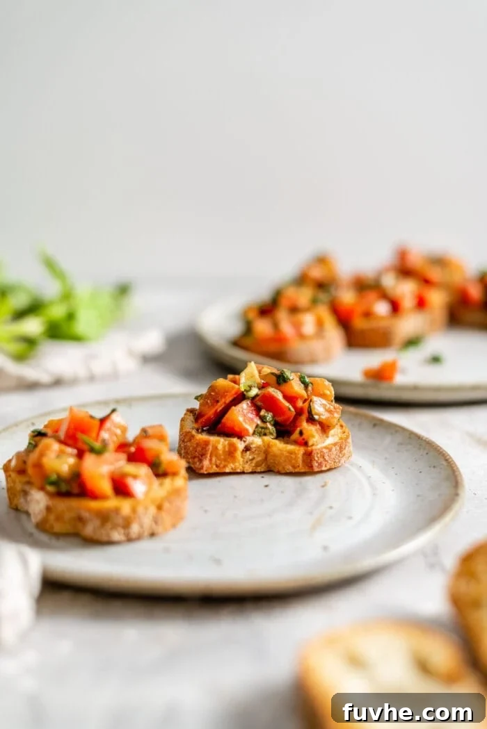 A single slice of perfectly toasted baguette topped with a fresh, vibrant tomato and basil mixture.
