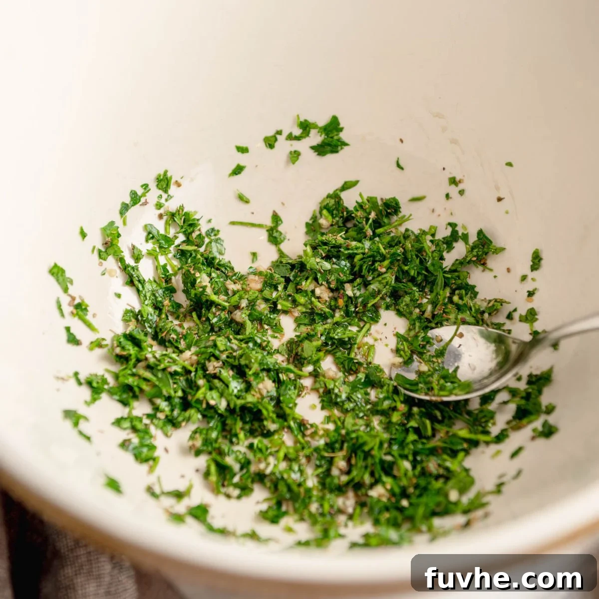 Plant-Based Greek Pasta Salad 5 Finely chopped parsley in a large mixing bowl with a spoon.