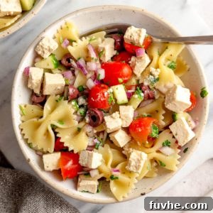 Plant-Based Greek Pasta Salad 8 Bowl of Greek pasta salad with cucumber, tomato, red onion, olives and tofu feta on a marble cutting board.