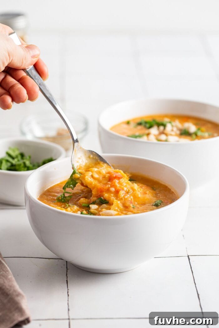 Hand using a spoon to take a spoonful of mulligatawny from a bowl, highlighting its texture.