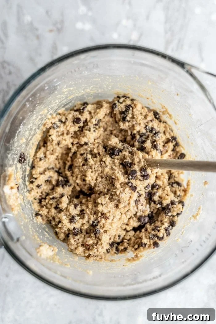 Plant-Powered Quinoa Chocolate Chip Cookies 5 Mixed chocolate chip quinoa cookie dough in a glass mixing bowl with a wooden spoon.