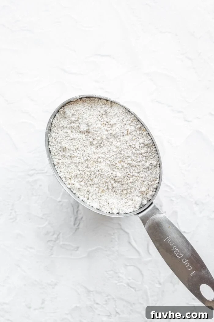 Metal measuring cup filled with freshly blended oat flour, showcasing its fine texture.