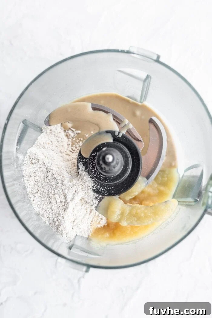 Oat flour, applesauce, and tahini combined in a food processor, ready to be blended into brownie batter.