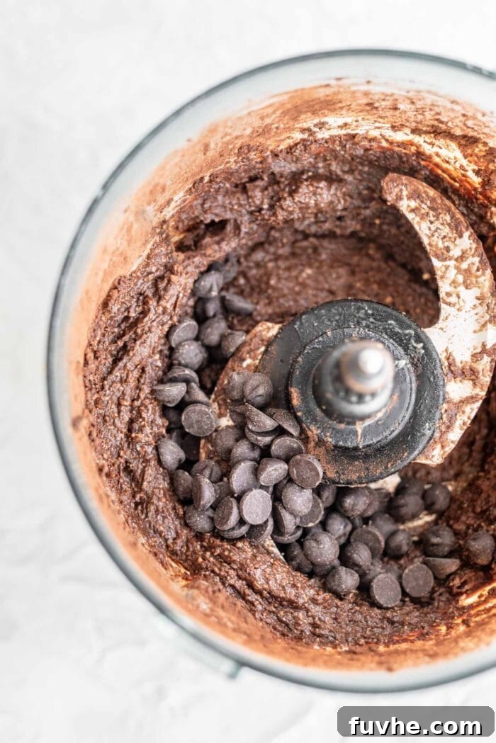 Thick chocolate brownie batter speckled with dairy-free chocolate chips inside a food processor bowl.