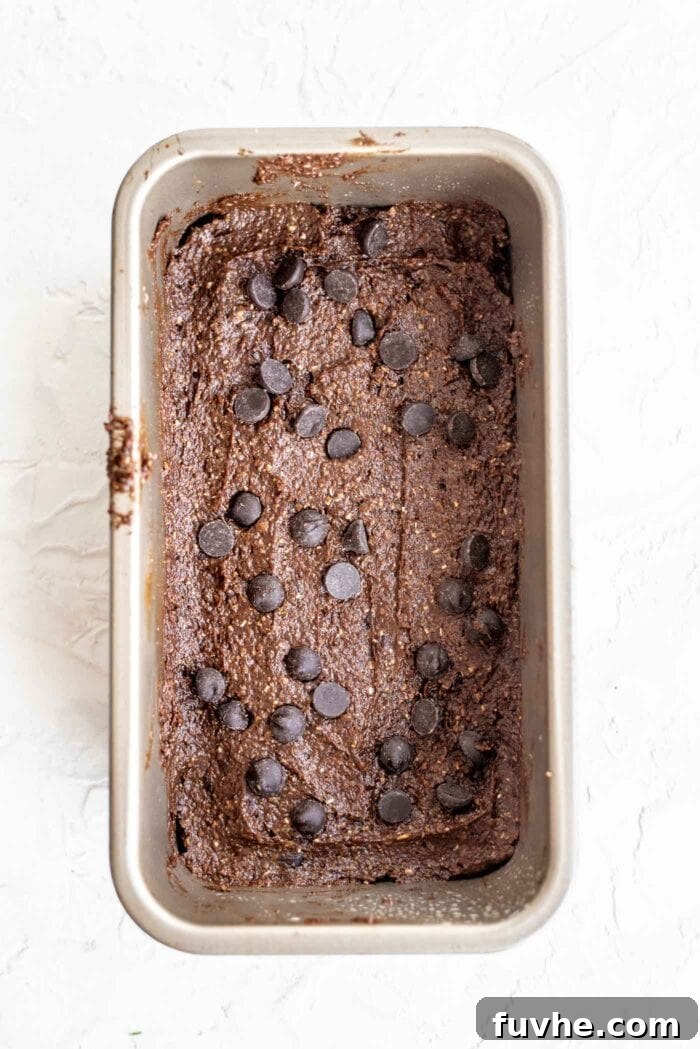 Smooth brownie batter topped with extra chocolate chips spread evenly in a prepared loaf pan, ready for baking.